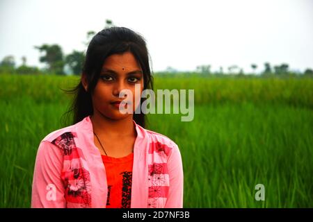 Nahaufnahme eines Teenagers in rosa Kleid, lange Haare, lächelnd und stehend auf einem Reisfeld mit grünen Pflanzen, selektive Fokussierung Stockfoto