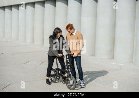 Fürsorglicher Mann, der Freundin hilft, eBike zu fahren und sie zu unterstützen. An einem sonnigen Herbsttag Stockfoto