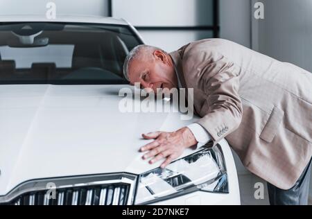 Fröhlicher alter Mann in formeller Kleidung steht vor Modernes weißes Auto Stockfoto