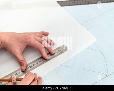 Schneiderhände zeichnen Muster Layout des Kleides mit Bleistift und Lineal auf Pauspapier aus Diagrammpapier zu Hause Stockfoto