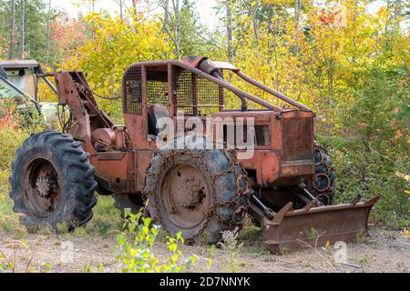 Ein alter, rostiger, verlassener schwerer Traktor mit Pflug vorne. Der Traktor befindet sich neben einem Wald. Ketten an Vorderreifen. Keine Kennzeichnungen. Stockfoto