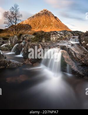 Berühmter Glencoe Wasserfall mit der Buachaille im Hintergrund. Aufgenommen an einem sonnigen Morgen mit Licht auf den Berggipfel. Stockfoto