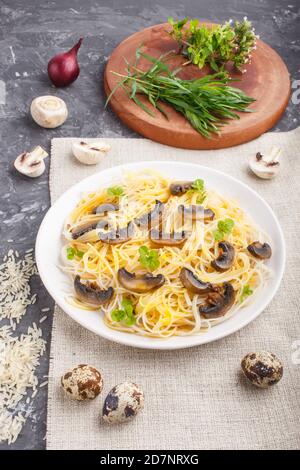 Reisnudeln mit Champignons, Eiersauce und Oregano auf weißem Keramikplatte auf schwarzem Betongrund. Seitenansicht, Nahaufnahme. Stockfoto