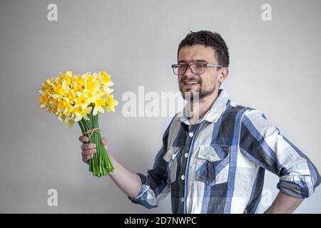 Ein junger Mann in Brille und Hemd mit Blumenstrauß. Auf hellem Hintergrund. Das Konzept der Grüße und Frauentag. Stockfoto