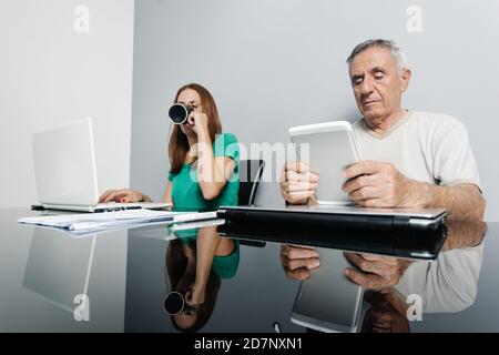 Mann und Frau mittleren Alters in legerer Kleidung mit digitalen Gadgets während der Arbeit zusammen aus der Ferne in modernen Arbeitsplatz im Home Office. Stockfoto