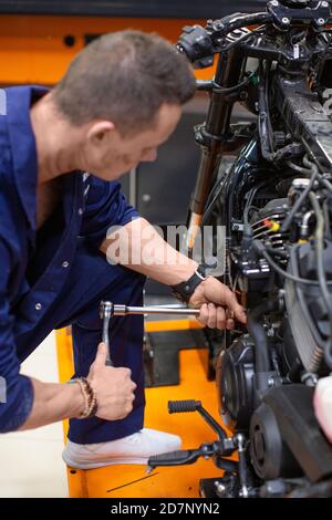 Vertikales Foto eines Mannes in einer Werkstatt repariert ein Motorrad. Konzentrieren Sie sich auf die Hände. Stockfoto