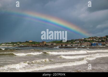 Dramatische Küstenlandschaft mit Regenbogen. Schöner Regenbogen gegen dunklen stürmischen Himmel in Gijon, Asturien, Spanien. Stockfoto