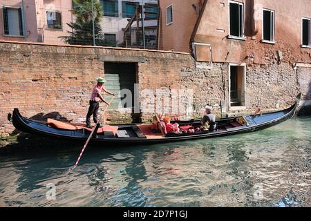 Gondolier nimmt Touristen mit seiner Gondel durch die Stadt an einem hellen Tag. Stockfoto