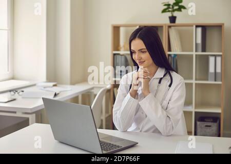 Die Ärztin sitzt vor einem Laptop und überprüft die Ergebnisse einer medizinischen Untersuchung. Stockfoto