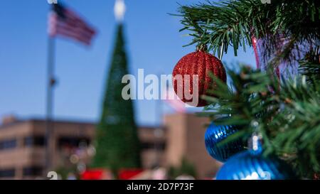 Rotes Glas Weihnachtsbaum Globus Ornament hängt von immergrün mit Blaue Glühbirnen unten und ein weiterer Baum im Hintergrund Stockfoto