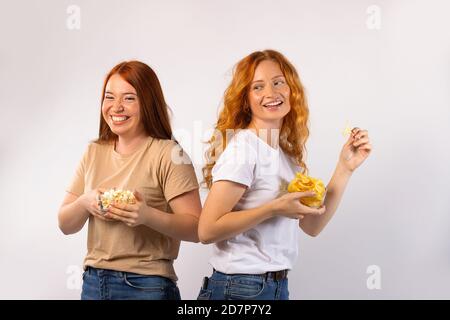 Schöne Zeit zu verbringen. Rothaarige Mädchen essen Chips und Popprn, lachen und lockern sich auf. Foto auf weißem Hintergrund. Stockfoto