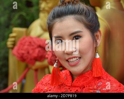 Schöne junge Thai Frau trägt ein rotes traditionelles chinesisches Spitzenkleid und lächelt für die Kamera während des chinesischen Neujahrs. Stockfoto