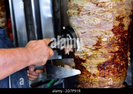 Giros, die im zypriotischen Restaurant Spieß einschalten, wobei der Koch sie benutzt Tragbares elektrisches Schnitzmesser zum Abschneiden von Scheiben für Kebab Stockfoto