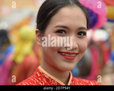 Kostümierte junge Teilnehmerin und Tänzerin mit Zahnspangen bei Bangkoks Chinese New Year Street Parade lächelt für die Kamera. Stockfoto