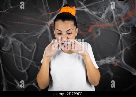 Junge schöne Frau auf schwarzem Hintergrund mit Spinnweben und Spinnen Schreien und Schreien laut mit den Händen am Mund Stockfoto