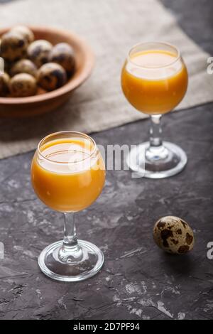 Süßer Eierlikör im Glas mit Wachteleiern auf schwarzem Betongrund. Seitenansicht, Low-Key, Nahaufnahme. Stockfoto