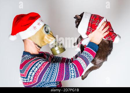 Person in Gasmaske und Weihnachtsmütze, die auf seine aufpassen Schwarze Weihnachtskatze Stockfoto