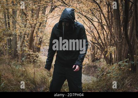 Ein beängstigender Kapuzenmann, der eine Pestdoktor-Maske trägt und in einem Wald steht. Stockfoto