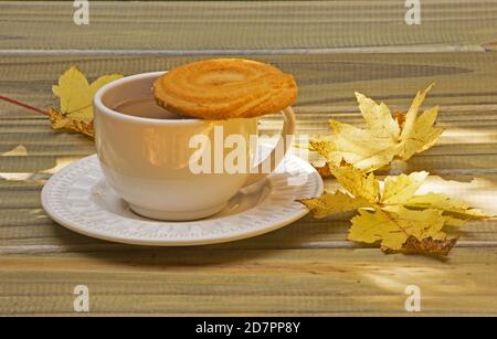 Eine Tasse Kaffee mit Keks und Herbstblättern auf einem Holztisch Stockfoto