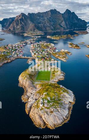 Luftaufnahme der Inselwelt in der Nähe des Fischerdorfes Henningsvaer, vor Halbinsel mit Fußballplatz, im hinteren Bergmassiv Vagakallen Stockfoto