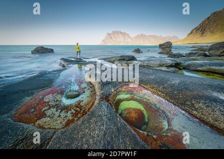 Frau, die auf Felsen am Strand steht, im Vorflurbecken mit Formation Eye of Utakleiv, Vestvavoy, Nordland, Lofoten, Norwegen Stockfoto