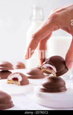 Teekuchen aus weich schmelzendem Marshmallow Zentrum, Erdbeermarmelade Füllung und Schokolade mit Milch im Hintergrund beschichtet Stockfoto