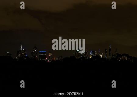 Nachtlandschaft von der Hauptstadt Australiens, Melbourne. Dunkler Park mit Bäumen und Lichtern auf den Skyscrappers. Stockfoto