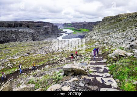 Dettifoss, Island - 16. Juni 2018: Wasserfall Flussschlucht mit bewölktem Himmel und Wasser mit felsigen Klippen und Menschen Wandern in Vatnajokull Nationa Stockfoto