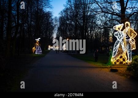 Warschau, Polen - 20. Dezember 2019: Beleuchtete Dekoration Lichter Girlande von Paar Statue in der Nacht Abend zu Weihnachten in Lazienki Park mit Menschen Stockfoto