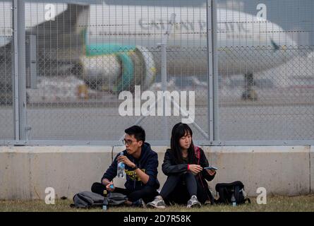 Ein Paar sitzt auf dem Rasen, als ein Flugzeug der Hongkonger Fluggesellschaft Cathay Pacific Airways auf der Start- und Landebahn des Hong Kong International Airport stationiert ist.Cathay Pacific eine Hongkonger Airline-Gruppe hat eine Unternehmensumstrukturierung als Reaktion auf die Wirtschaftskrise COVID-19 angekündigt, die 8,500 reduzieren wird Jobs und schloss seine regionale Fluggesellschaft Cathay Dragon. Stockfoto