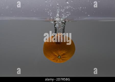 Nahaufnahme der bunten Mandarine fallen in Wasser auf grauem Hintergrund. Wunderschöne Hintergründe. Stockfoto