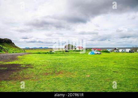 Seljalandsfoss, isländischer Wasserfall mit grüner, üppiger Sommerlandschaft und Häusern an bewölkten Tagen mit Campingzelten und Parkplatz Stockfoto