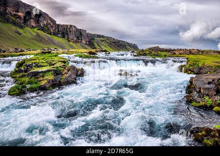 Landschaftsansicht des rauschenden Flusses durch Fjadrargljufur Canyon in Island Mit Stromschnellen Strom von Wasser durch grünes Gras Moos und wolkiger Himmel Stockfoto