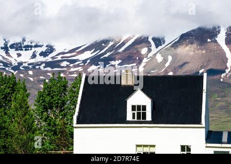 Blick auf Sulur bei Akureyri mit wolkenverhangendem Himmel und Nahaufnahme von Bauernhaus und schneebedeckten Bergen Stockfoto