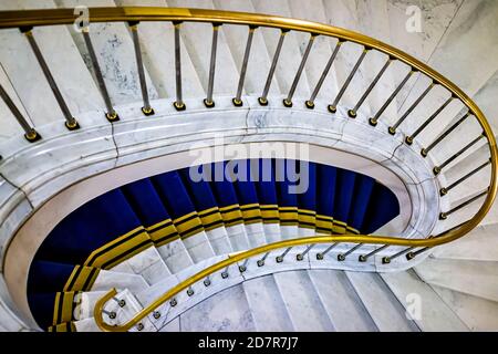 Blick nach unten aus einem hohen Winkel auf eine Wendeltreppe aus Marmor oder Treppen mit goldenem Retro-Geländer und blaugelbem Teppich in Warschau, Pola Stockfoto