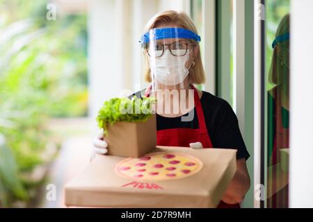 Die Lieferung von Lebensmitteln ist gesperrt. Essen während des Coronavirus-Ausbruchs mitnehmen. Restaurantbesitzer in Gesichtsmaske hält Pizza und Salat-Box. Bleib zu Hause und sei saf Stockfoto