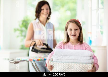 Frau und Kind bügeln Kleidung. Mutter und Tochter faltet Kleidung beim Bügelbrett. Mutter und Kind putzen Haus. Hausarbeiten. Stockfoto