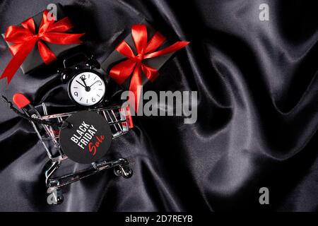 Uhr im Warenkorb mit schwarzem Anhänger und Geschenken auf schwarzem Stoffhintergrund. Black friday Konzept. Stockfoto