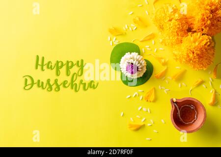 Diya-Lampen aus Ton, die während der Dussehra mit gelben Blüten, grünem Blatt und Reis auf gelbem Hintergrund leuchten. Dussehra Indian Festival Konzept. Stockfoto