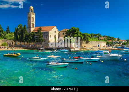 Wunderschöne Bucht mit Strand und Booten. Spektakuläre Gehweg und Steinkirche mit Turm an der Küste, Hvar, Insel Hvar, Dalmatien, Kroatien, Europa Stockfoto