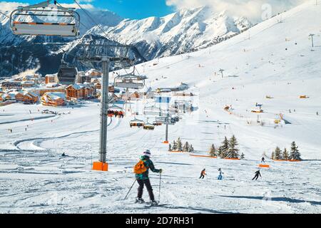 Leichte Skipisten mit trainierenden Skifahrern. Französisches Skigebiet mit Skiliften, Seilbahnen und Holzgebäuden im Hintergrund, Alpe d Huez, Frankreich, Europa Stockfoto