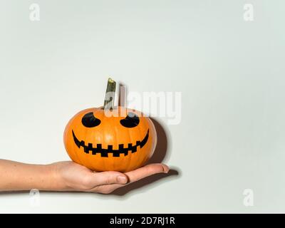 Halloween Kürbis in der Hand auf weißem Wandhintergrund. Halloween-Konzept mit Platz für Text oder Design. Hartes Licht. Jack-o-Laterne lachendes Gesicht auf orangefarbenem Squash Stockfoto
