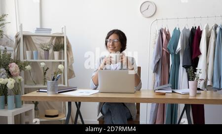 Glückliche junge Designerin sitzt am Schreibtisch und träumt davon Stockfoto