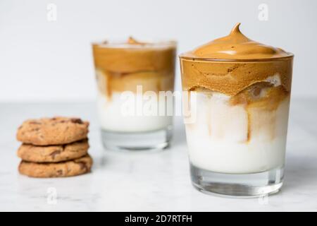 Zwei Dalgona Kaffeegläser mit Schokoladenkeksen auf Marmor Tabelle Stockfoto