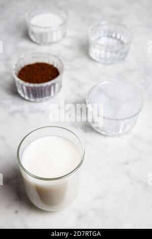 Dalgona Kaffeezutaten auf einem Marmortisch: Instant-Kaffee, Milch, Zucker, Wasser und einige Eiswürfel Stockfoto