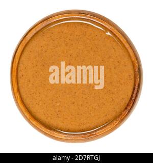 Mandelbutter in einer Holzschüssel glatt streichen. Speisepaste aus gemahlenen Mandeln zu einer Nussbutter. Püree der Nüsse von Prunus dulcis. Nahaufnahme. Stockfoto