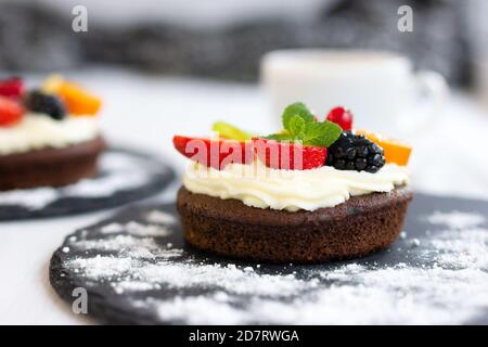 Schokoladen-Cupcakes mit Frischkäse, Obst und Beeren. Biscuit Mini Cake mit Puddingcreme als Kaffee-Dessert. Nahaufnahme, Seitenansicht Stockfoto