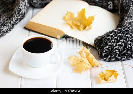 Gelbe Herbstblätter, Kaffeetasse, warmer Strickschal mit geöffnetem alten Buch auf weißen Holzbrettern. Gemütliches Haus Lesen, Hygge Konzept Stockfoto