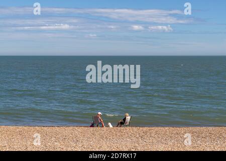 Zwei Frauen sitzen auf Liegestühlen am Steinstrand von Aldeburgh, Woodbridge, Suffolk, Großbritannien. Stockfoto