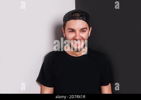 Urban Style junger Mann lächelnd glücklich, lehnte sich gegen schwarz-weiße Wand. Textort. Stockfoto
